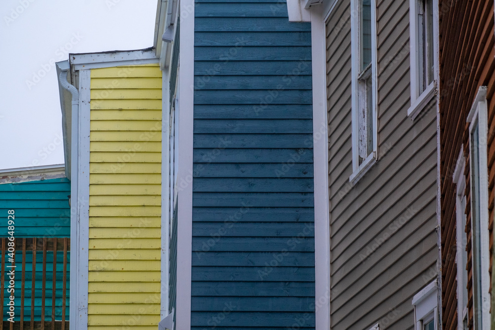 The top corners of five wooden buildings or houses in a step formation. All the buildings have bright coloured wood horizontal clapboard siding with double hung windows and white trim under a grey sky The top corners of five wooden buildings or houses in a step formation. All the buildings have bright coloured wood horizontal clapboard siding with double hung windows and white trim under a grey sky