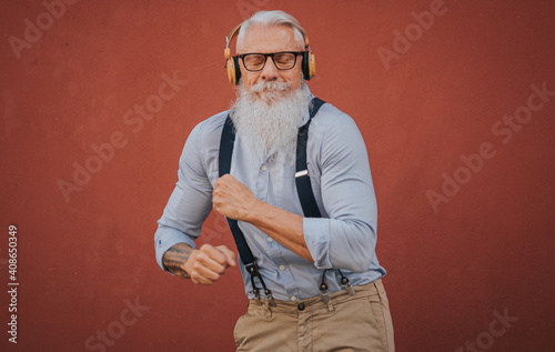 an older man in hipster clothes and glasses and long white beard listens to music and dance happily in the street focus on head