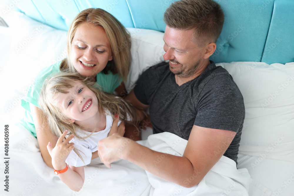 Obraz premium Parents with child indulge and cuddle in bed. What is use of parental hugs for child concept