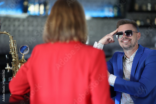 Smiling confident man in sunglasses meets woman near bar counter. Narcissistic personality disorder in men concept