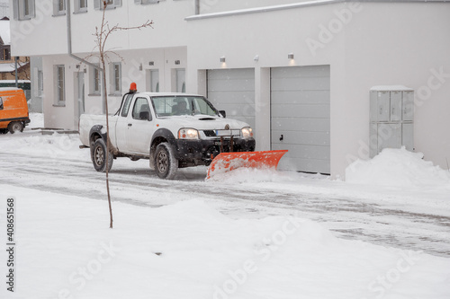 A pickup truck equipped with a plow is removing snow from a sloped driveway in winter. White pickup truck with plow. Clearing the streets from snow.