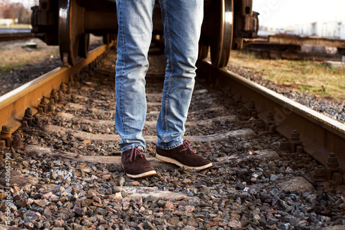 Male feet in blue jeans and brown boots stand on the railway tracks in autumn