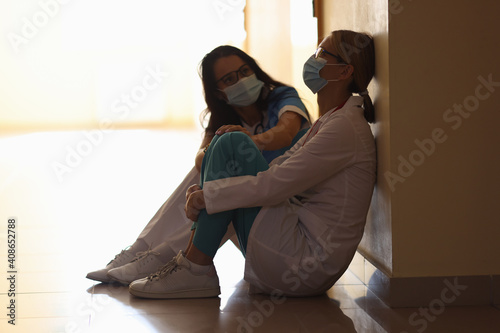 Two doctors in medical protective masks sit in corridor of medical facility. Medical error during operations concept photo