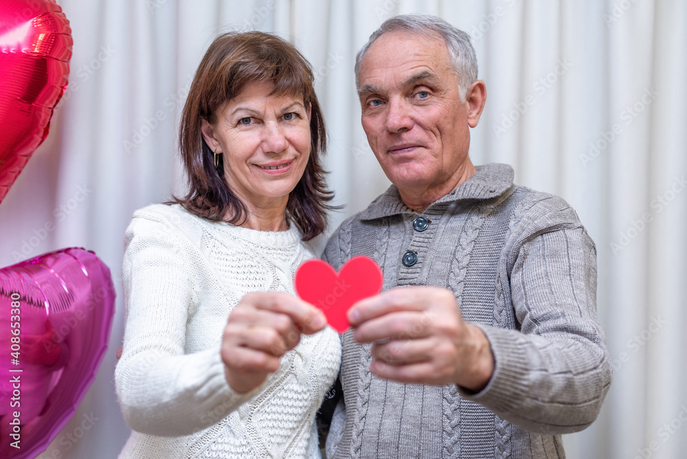 Happy couple seniors celebrate Valentine's Day. Man and woman hold red heart in hands and smile. Romantic relationships, love and dating in retirement. Lifestyle of elderly people. Mature pensioners Happy couple seniors celebrate Valentine's Day. Man and woman hold red heart in hands and smile. Romantic relationships, love and dating in retirement. Lifestyle of elderly people. Mature pensioners