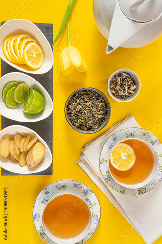 Wallpaper Mural Green and herbal tea with lemon,lime and ginger.Two porcelain  cups, teapot and beautiful flowers on yellow background. Top view. Torontodigital.ca