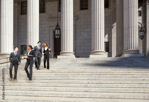 Four well dressed professionals walk down steps in discussion outside of a courthouse. Could be lawyers, business people etc.
