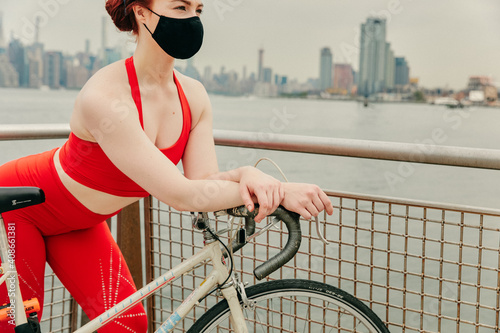Young female cyclist wearing face mask with bike by waterfront
