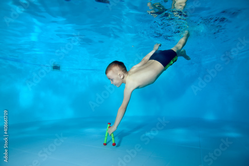A picture of a sporty boy who dives to the bottom of the pool for a toy. Fun dives underwater. Active happy child. Swimming classes. Bodily exercises. Healthy lifestyle.