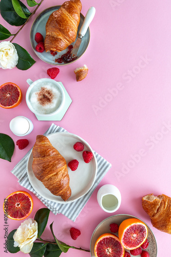 Flat lay of a breakfast scene with croissants, fruit and cappuccino on pink background