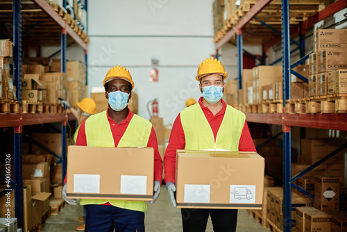 Multiracial warehouse workers holding delivery boxes while wearing safety mask for coronavirus prevention - Focus on faces