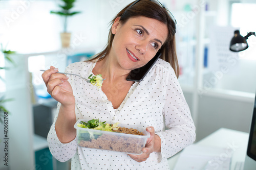 woman eating salad and taking call on smartphone photo