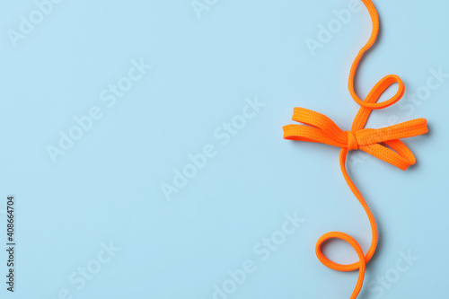 Orange shoelace on light blue background, top view. Space for text photo