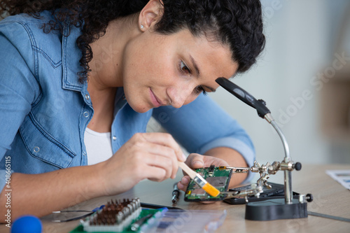woman cleaning electronics components with brush under a magnifying-glass