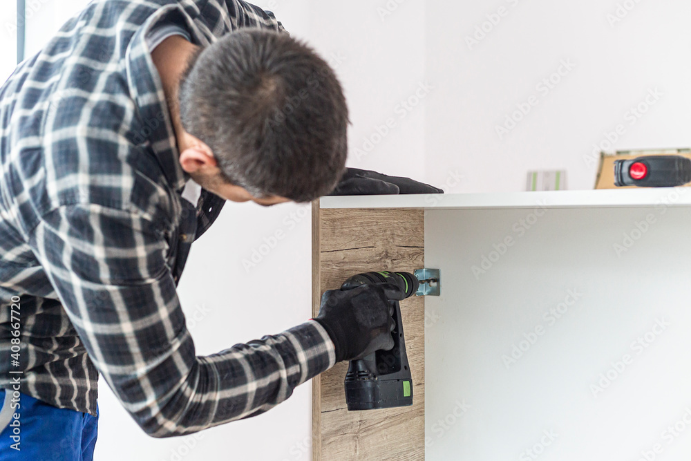 A carpenter drilling holes in a kitchen shelf