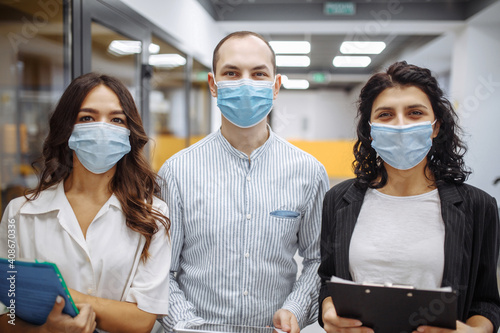 Portrait of three office workers wearing medical masks discussing business and future prospects. New normal, health care, office hygiene concept. Coronavirus quarantine, pandemic, spread prevention.