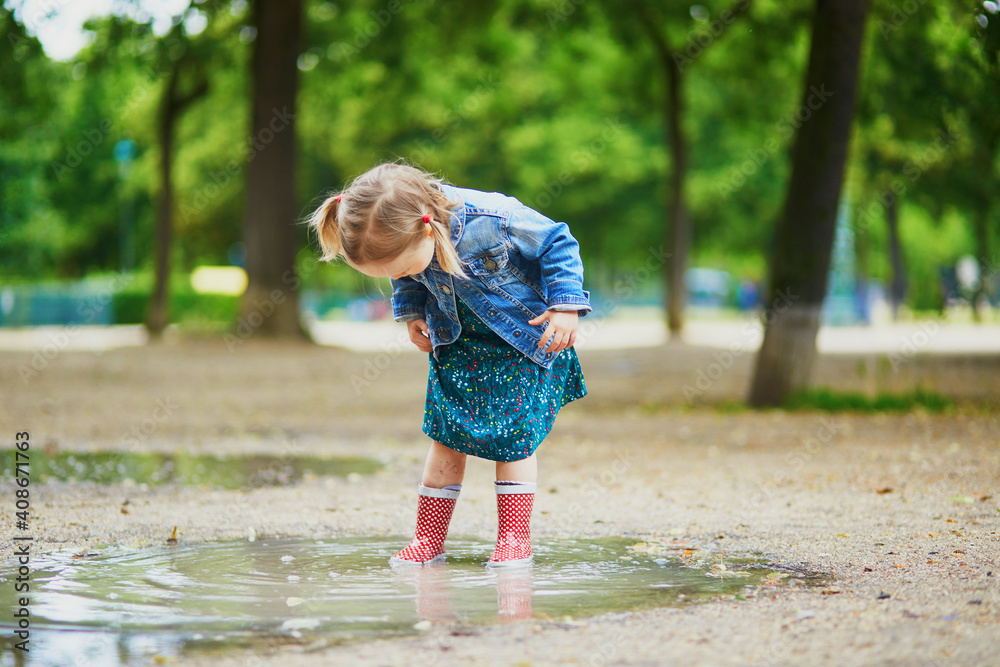 Naklejka premium Child wearing red rain boots and jumping in puddle on a summer day