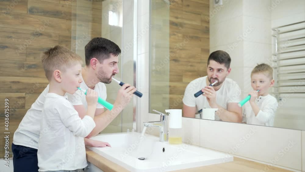 Father with little cute son brushing teeth in bathroom. Сheerful Dad and a funny child boy in the morning in front of the mirror wash together. Fathers Day. Young family Father with little cute son brushing teeth in bathroom. Сheerful Dad and a funny child boy in the morning in front of the mirror wash together. Fathers Day. Young family