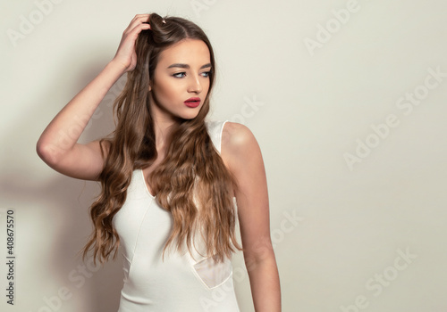 Beautiful young woman with long shiny and healthy hair posing in dress on grey background