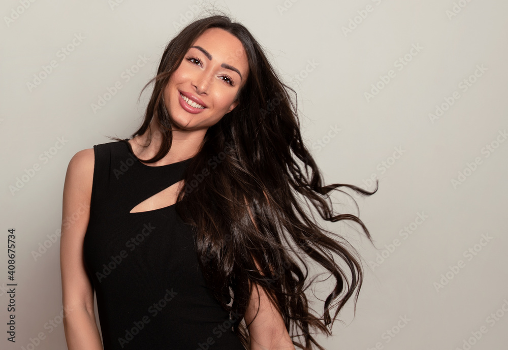 Beautiful young woman with long shiny black hair and natural make-up posing in dress on grey background Beautiful young woman with long shiny black hair and natural make-up posing in dress on grey background