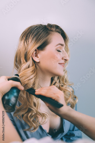 Stylist spraying hair of a female client at the beauty salon - hairstylist at work. Close up of hairstyle artist doing young lady clients hair.