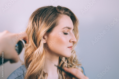 Stylist spraying hair of a female client at the beauty salon - hairstylist at work. Close up of hairstyle artist doing young lady clients hair.