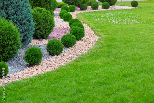 Landscape bed of garden with wave ornamental growth cypress bushes gravel mulch by color rock way on a day spring park with green lawn meadow, nobody..