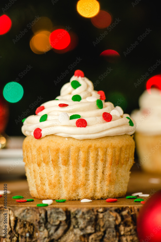 Vanilla cupcake with buttercream icing and christmas colored sprinkles on a wooden table Vanilla cupcake with buttercream icing and christmas colored sprinkles on a wooden table