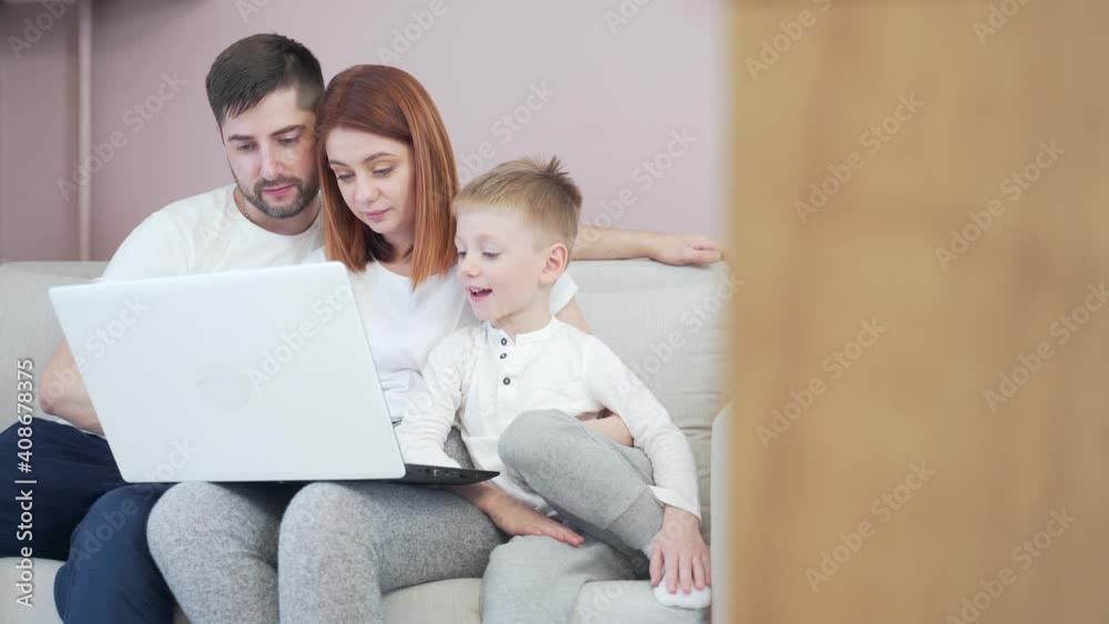 young happy family dad and mom with young children communicates online on laptop remotely. Waving hands and laughing sitting on the couch in the living room or kitchen at home talking to grandparents young happy family dad and mom with young children communicates online on laptop remotely. Waving hands and laughing sitting on the couch in the living room or kitchen at home talking to grandparents