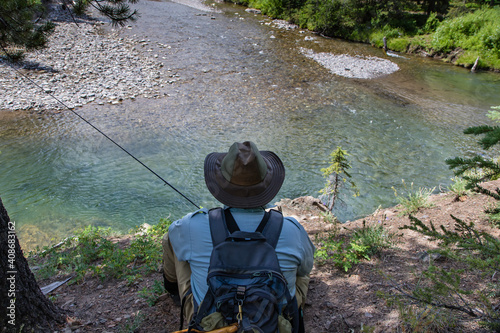 Solitary Fly-fisherman sits and observes a pool on a freestone river prior to commencing fishing in the Rocky Mountains of Alberta