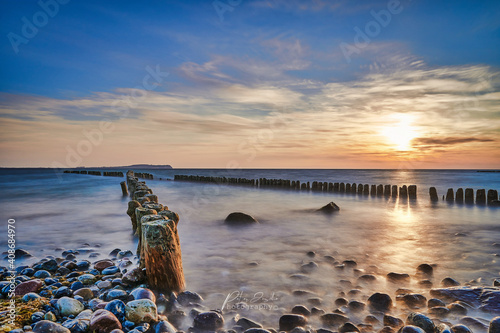 sunset at the baltic sea with cross groynes, stones and clouds. beautiful frbenfroher sky, long time exposure 