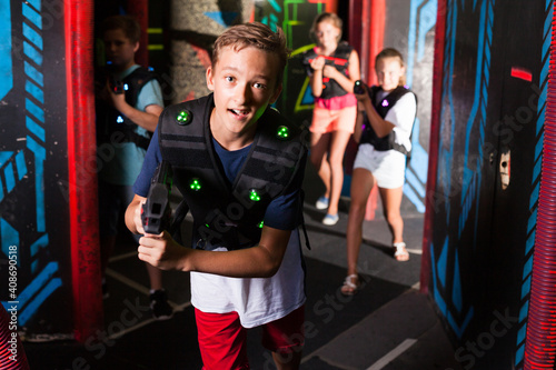 Excited boy aiming laser gun at other players during lasertag game in dark room..