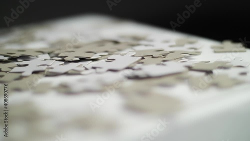 Close up of white and gray puzzle pieces falling in slow motion on a white surface and bouncing off with a dark background. Shot in 4K with shallow depth of field. Smooth sliding movement. photo