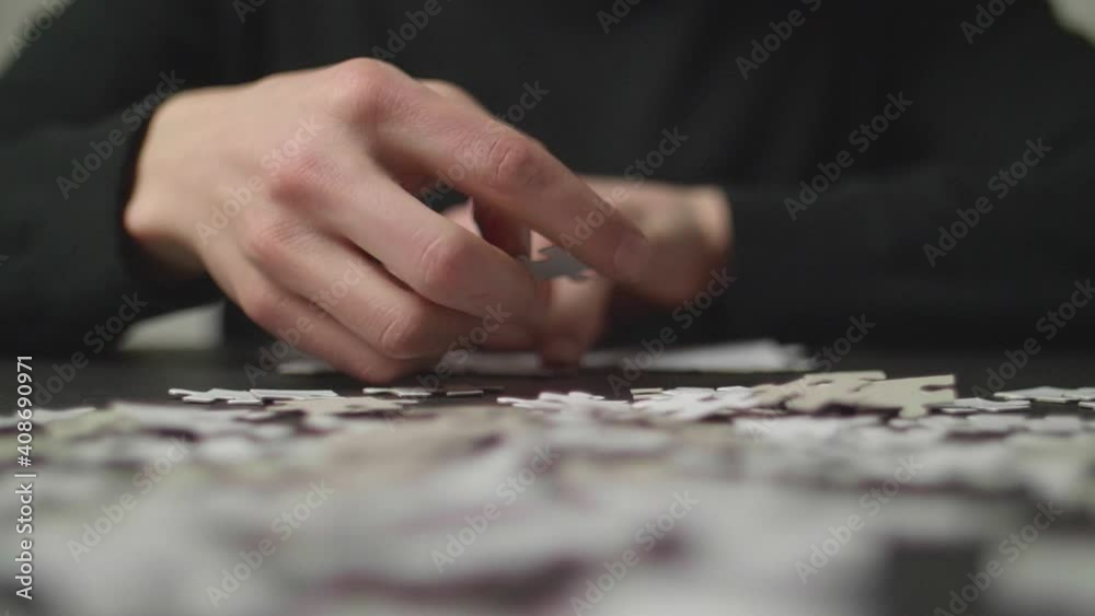 Puzzle pices falling on a table with a person's hands trying to solve the puzzle in the background. Shot in 4K, Slow Motion with Shallow Depth of Field. Puzzle pices falling on a table with a person's hands trying to solve the puzzle in the background. Shot in 4K, Slow Motion with Shallow Depth of Field.