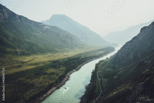 Misty mountain landscape with wide mountain river. Dark green gloomy scenery with confluence of two mountain river in mist. Dark atmospheric view to confluence of great rivers in rainy weather.
