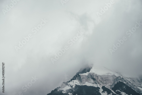 Minimalist monochrome atmospheric mountains landscape with big snowy mountain top in low clouds. Awesome minimal scenery with glacier on rocks. Black white high mountain pinnacle with snow in clouds. © Daniil