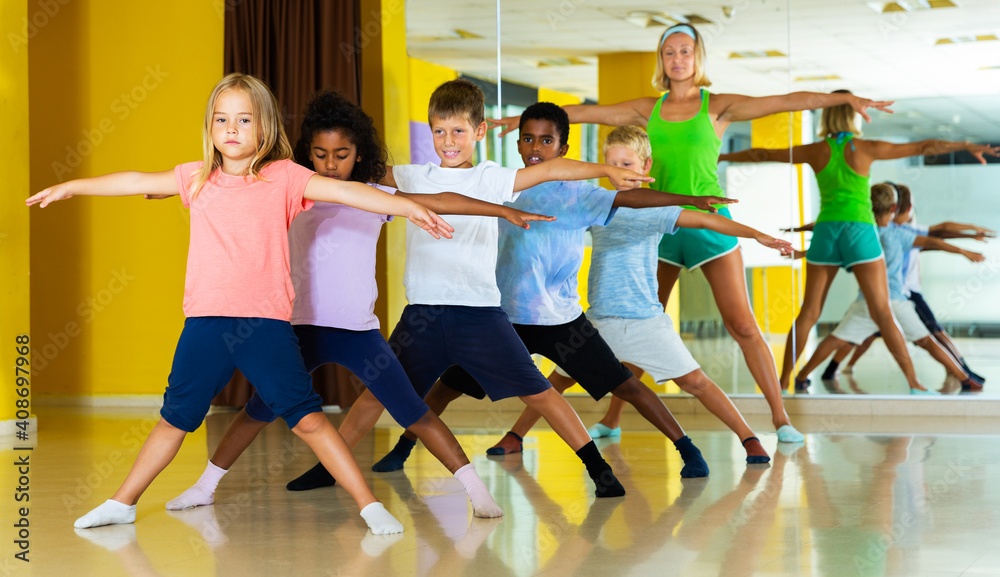 Group of tweens training movements of modern dance in choreography studio with female tutor