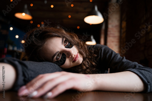 a girl with black curly hair and patches under her eyes lies on a table in a public place