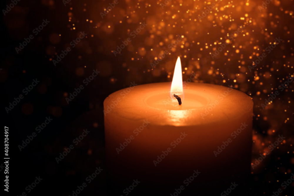 A candle burns in the dark against a background of golden bokeh