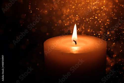 A candle burns in the dark against a background of golden bokeh