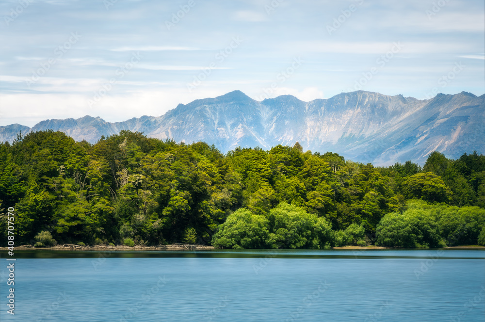 Lake Te Anau with the rainforest in the middle ground coming up to the water's edge and beautiful mountain peaks in the background in Fiordland National Park, New Zealand, South Island.