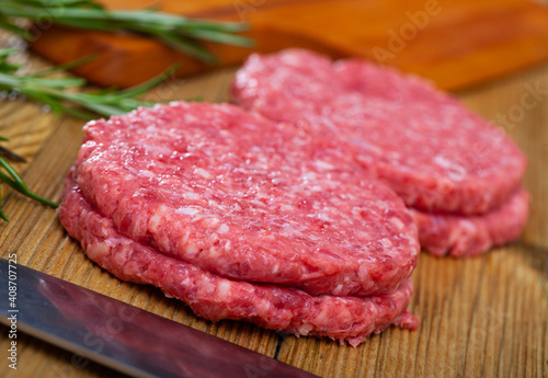 Raw formed hamburger patties ready for frying on wooden table with greens