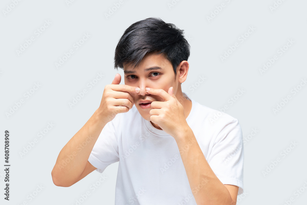 A handsome young Asian man squeezes a pimple on the tip of his nose. A handsome young Asian man squeezes a pimple on the tip of his nose.