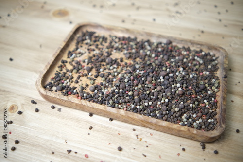 A mixture of Indian seasonings is poured into a wooden plate on a wooden table. Black pink pepper. Ingredients for the dish