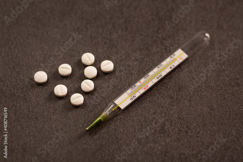 a handful of pills and a thermometer on a dark background