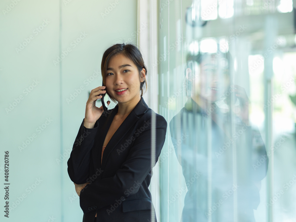Businesswoman talking on the phone while standing in glass partition office room Businesswoman talking on the phone while standing in glass partition office room