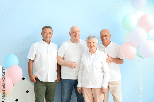 Senior people with balloons near color wall in room