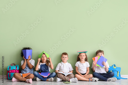 Little children with books sitting on floor against color background