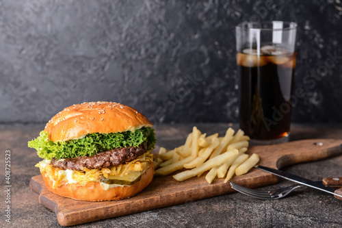 Board with tasty burger, french fries and cola drink on dark background