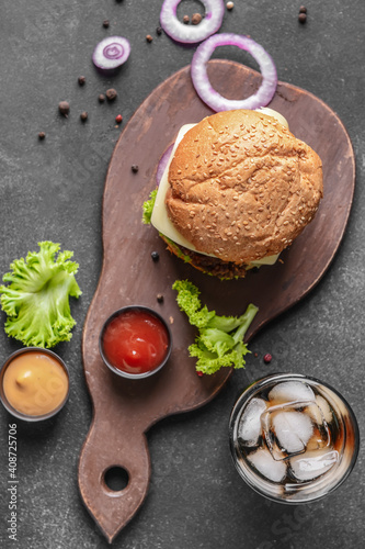 Board with tasty burger and cola drink on dark background