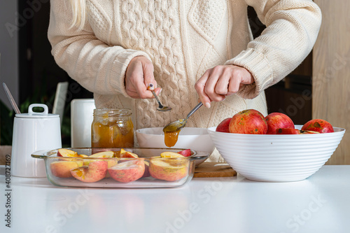 female with spoon pouring apples with honey in a glass container and prepare them for cooking